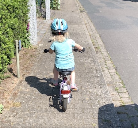 Enkelin lernt mit Helm das Fahrradfahren in einer ruhigen Seitenstraße in Ellerbek