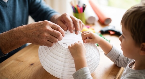 Opa und Enkelkind setzen gemeinsam den Drahtspanner in den weißen Papierlampion ein