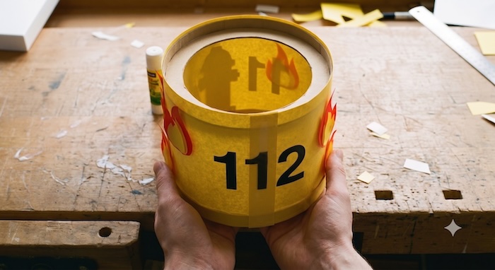 Gelbe Banderole um die Käseschachtel gelegt und zum Zylinder verbunden – die Feuerwehr-Laterne mit der 112 nimmt Form an