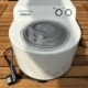 Weiße Eismaschine Nemox Gelatissimo mit zwei Drehknöpfen und durchsichtigem Deckel auf einem Holztisch im Garten