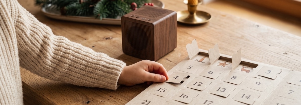 Holzlautsprecher neben einem Papier-Adventskalender, eine Kinderhand öffnet ein Türchen