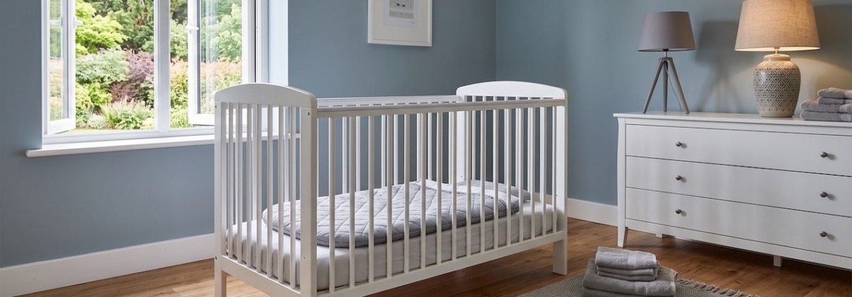 Leeres Kinderbett mit fester Matratze, Laken und ausgebreitetem Babyschlafsack, ohne Kissen und Kuscheltiere