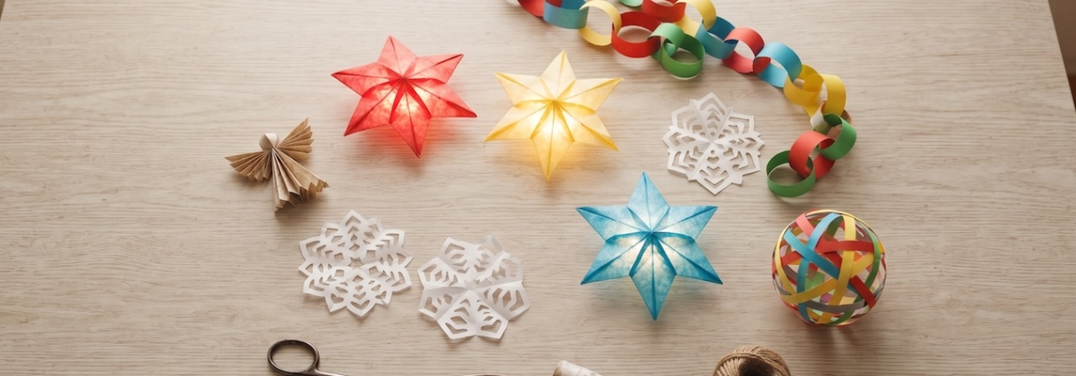 Küchentisch von oben mit fertigem Weihnachtsschmuck aus Papier: Sterne, eine Papierkette, Schneeflocken und ein Engel