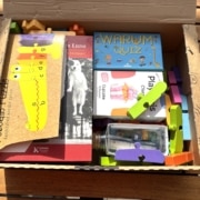 Offener Karton mit Holzpuzzle, Büchern, Quizspiel und Bauklötzen — ein gepacktes Paket für das Enkelkind in Südtirol