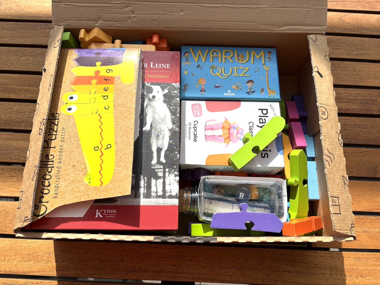 Offener Karton mit Holzpuzzle, Büchern, Quizspiel und Bauklötzen — ein gepacktes Paket für das Enkelkind in Südtirol