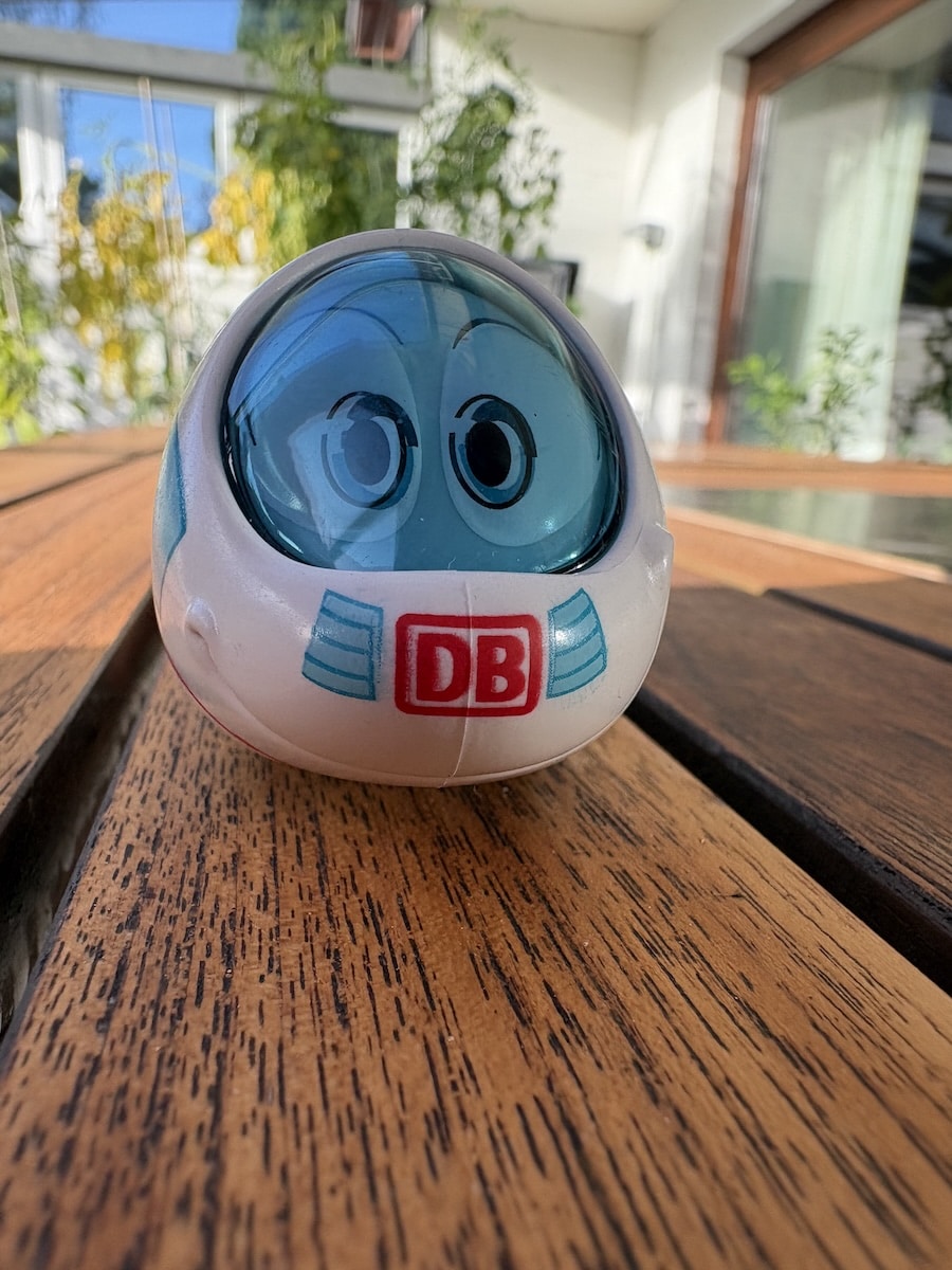 Spielfigur „Der kleine ICE“ mit großen blauen Augen auf einem Holztisch